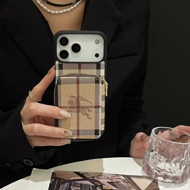 Person holding a phone with a plaid case, sitting at a table with a glass.