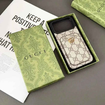 Beige GG monogram design case in its original green presentation box, showing the stitched rear card pocket, gold-coloured GG emblem and dark camera recess.