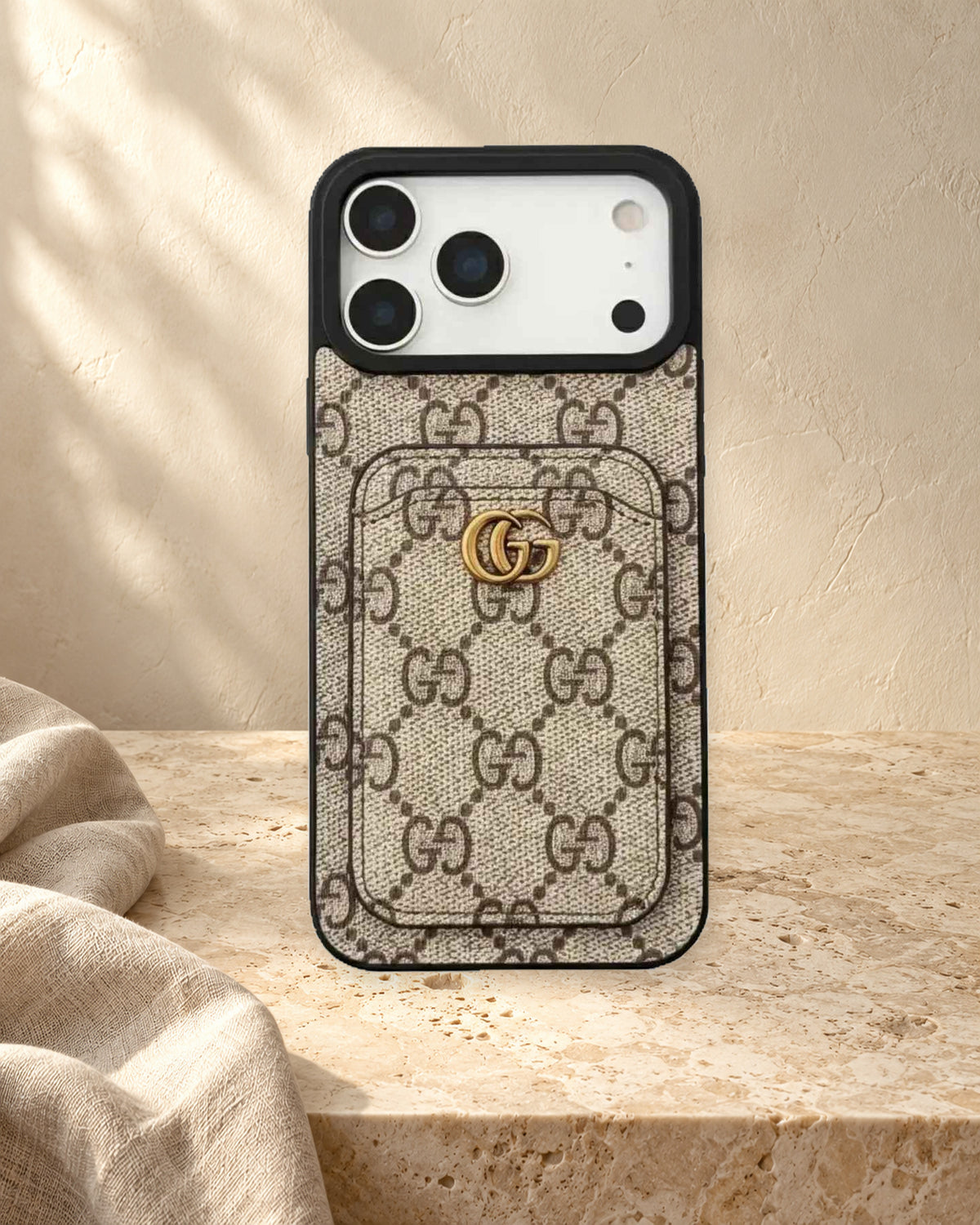 Beige GG monogram design iPhone case with a rear card pocket, gold-coloured GG emblem and a display phone in a warm ivory setting.