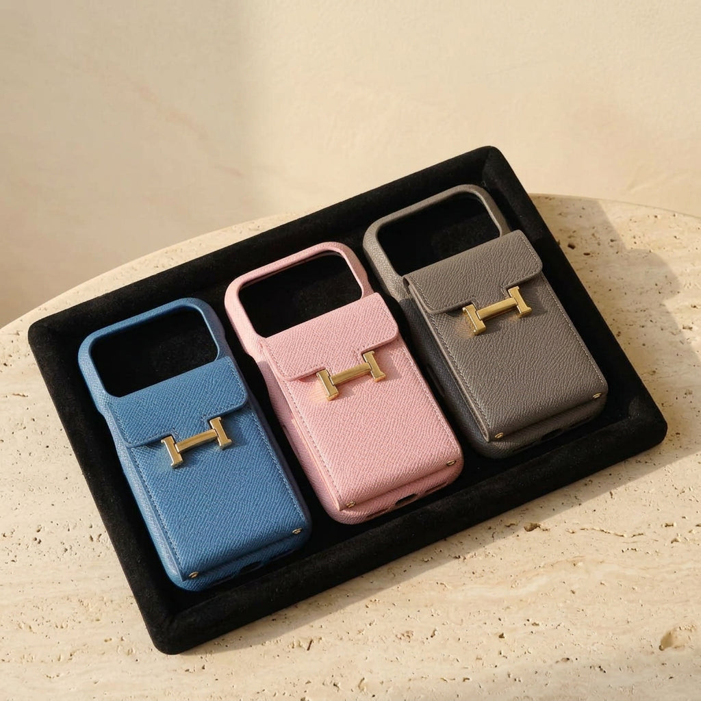 Blue, pink and grey H buckle design iPhone cases in a black tray on cream travertine.