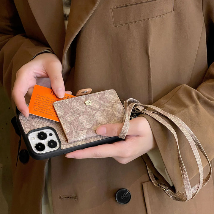 Phone case with Coach logo held by a hand Person holding a phone case with a card and wallet, wearing a brown coat.