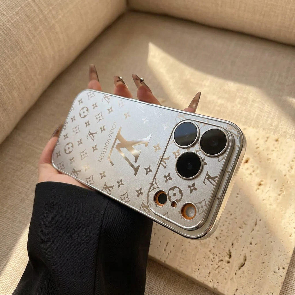 Silver Louis Vuitton monogram design iPhone case resting horizontally on a black-sleeved hand, with the wide camera surround on the right and large LV motif across the back.