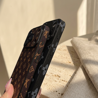 Two overlapping textured monogram iPhone cases viewed along their sides, one brown with small gold motifs and one black with large grey motifs.