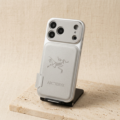 Silver Arc'teryx skeletal-bird design iPhone back cover upright on a black display stand, showing its textured rear panel, small side tab and wide camera surround.