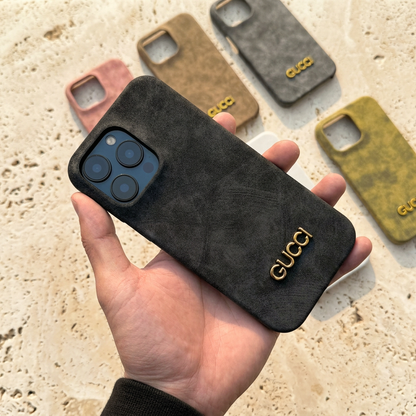 Black mottled Gucci design case held diagonally in a hand with a black sleeve, fitted to a blue display phone with other colour cases behind.