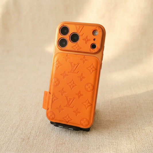 Upright Orange Louis Vuitton tonal monogram design iPhone case on a black display stand, showing a textured rear panel, patterned camera surround and side name tab.