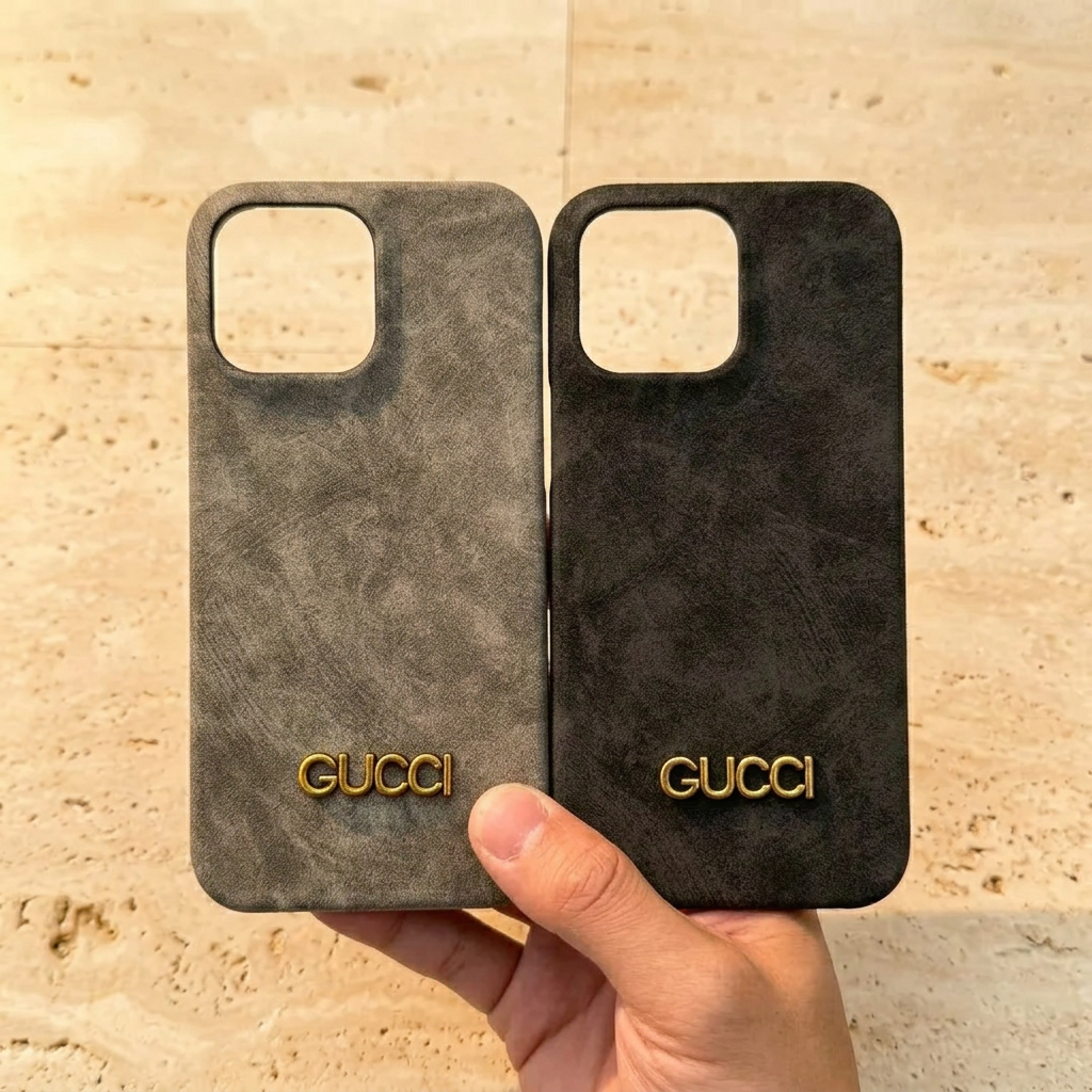 Hand holding gray and black mottled Gucci design back covers side by side, with gold-tone names and empty square camera openings.