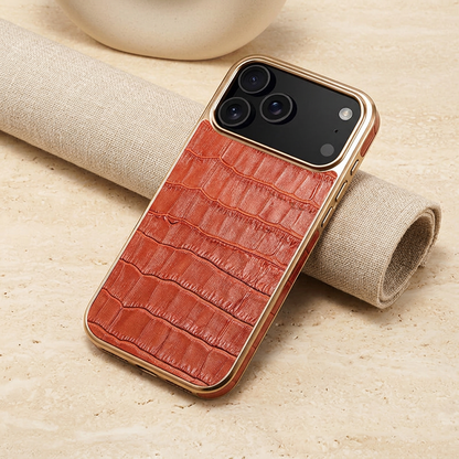 Wider diagonal view of the reddish-brown croc-pattern case across rolled neutral linen, with its gold-tone frame visible.