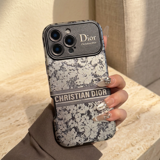 Grey-and-ivory floral iPhone case held upright, showing the Christian Dior band and textured camera panel.