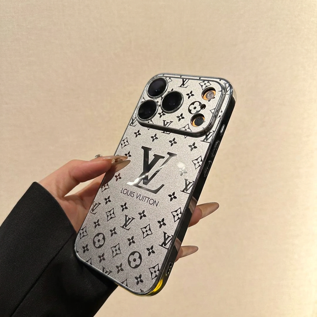 Silver Louis Vuitton monogram design iPhone case held at an angle, showing a wide patterned camera panel, large LV motif and dark reflective side rim with control details.