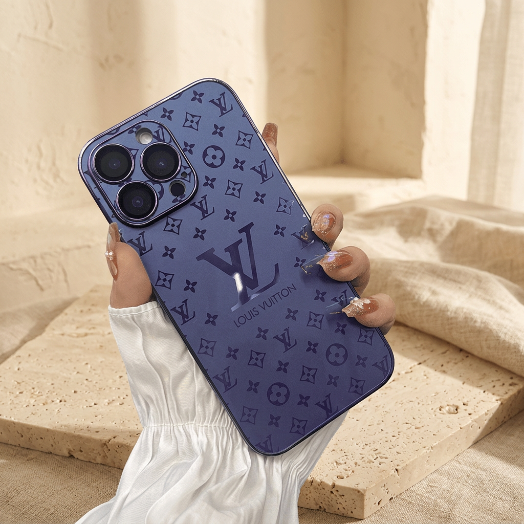 Blue Louis Vuitton monogram design iPhone case held diagonally by a white-sleeved hand with decorated nails, showing deeper blue floral motifs and a large central LV detail.