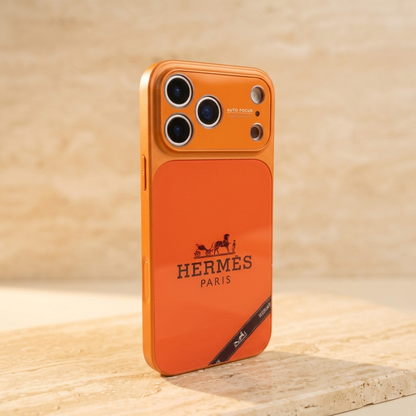 Style B orange Hermès design case standing at an angle with a black horse-and-carriage motif, name detail and diagonal black ribbon graphic near the bottom.