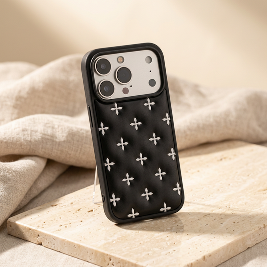 Crossquilt Puffy Faux Leather iPhone Case – Contrast Cross Design, Black case with white cross motifs shown at an angle against warm cream linen.