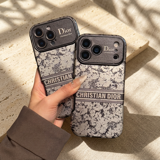 Two grey-and-ivory Christian Dior floral design iPhone cases held together, showing differing camera opening layouts.